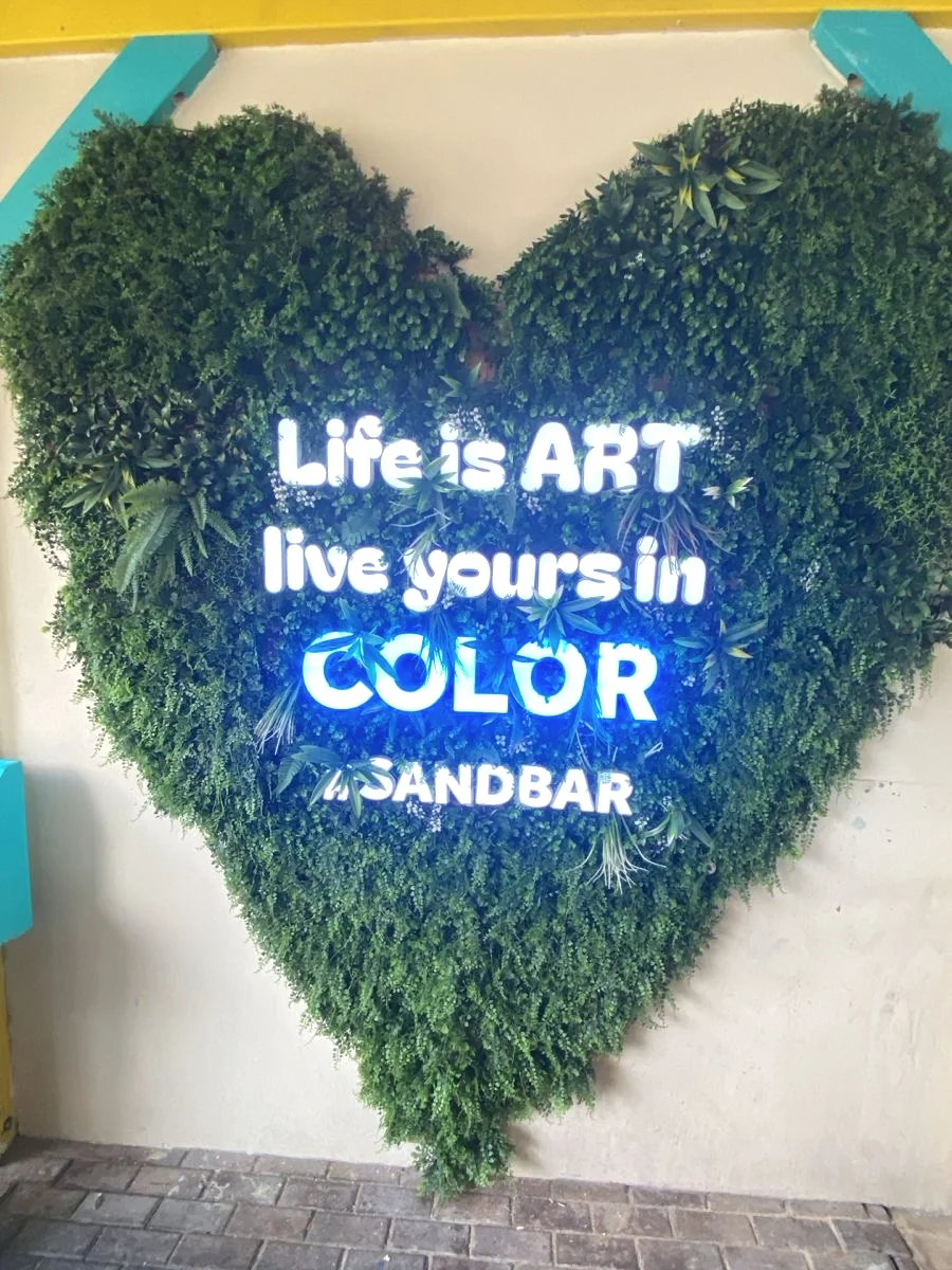 Illuminated lettering on a foliage wall.